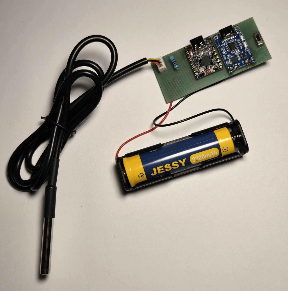 A built Setpoint kit laid out: the carrier board with its ESP32-C3 and TP4056 charger, the waterproof stainless DS18B20 probe on its lead, and an 18650 cell in its holder.